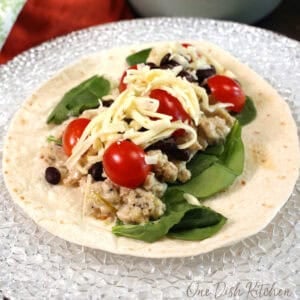 a single southwest chicken wrap on a white plate with tomatoes and spinach.