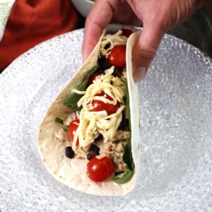 a southwest chicken wrap held together by a hand over a white plate