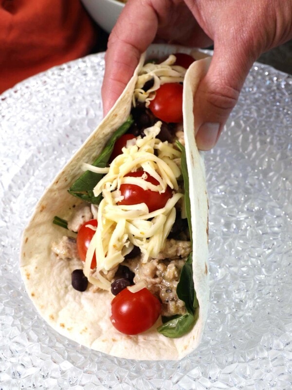 a southwest chicken wrap held together by a hand over a white plate