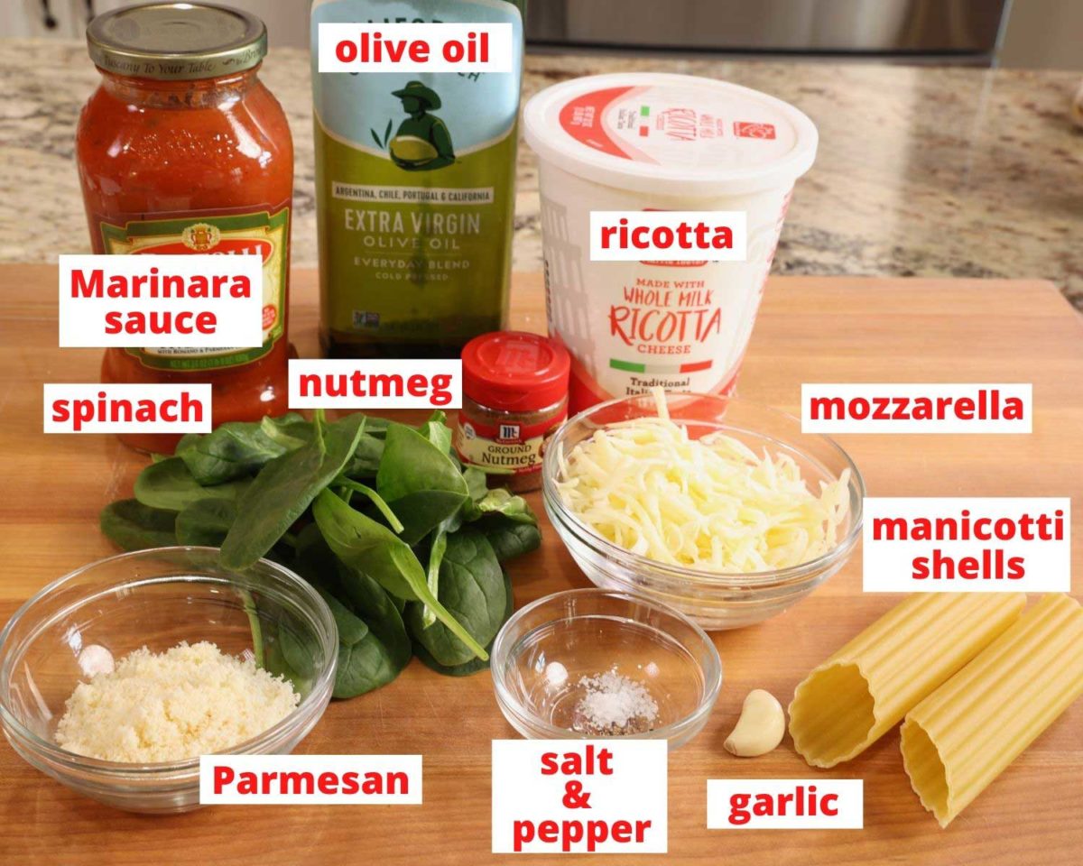 ingredients needed to make spinach manicotti all on a wooden cutting board: noodles, spinach, ricotta, cheeses, and olive oil.
