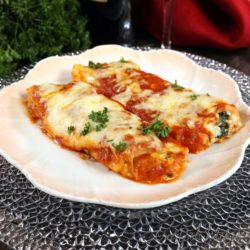 Two ricotta and spinach stuffed cannelloni noodles on a white plate.