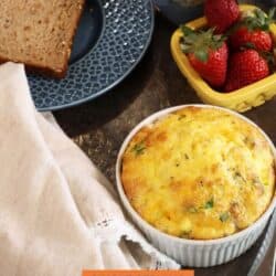 a bacon egg and cheese cup on a kitchen table next to a bowl of strawberries.