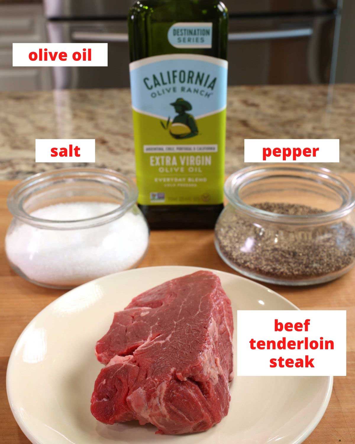a beef tenderloin steak on a white plate next to jars of salt and pepper and a bottle of olive oil.