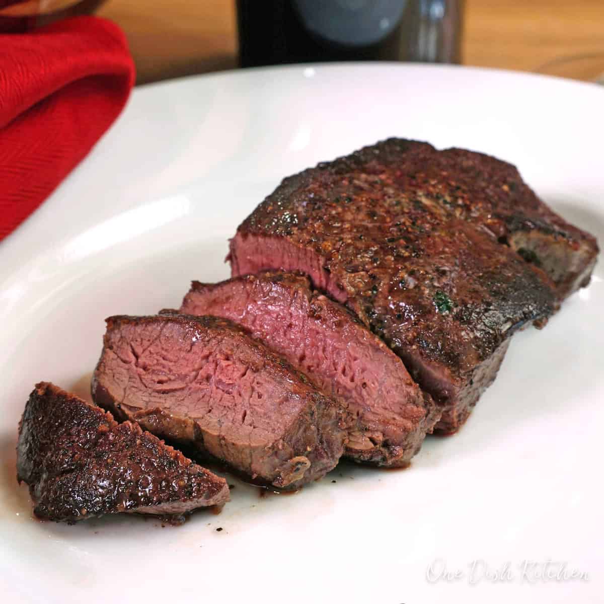 a small beef tenderloin steak sliced and on a white plate.