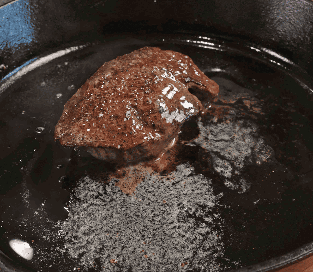 melted butter on top of a piece of steak in a black skillet.