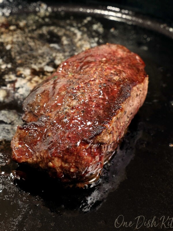a filet of beef in a cast iron skillet with melted butter over the top