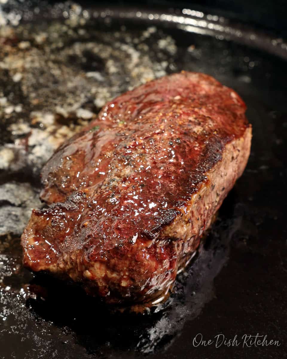 a beef tenderloin steak cooking in a cast iron skillet.