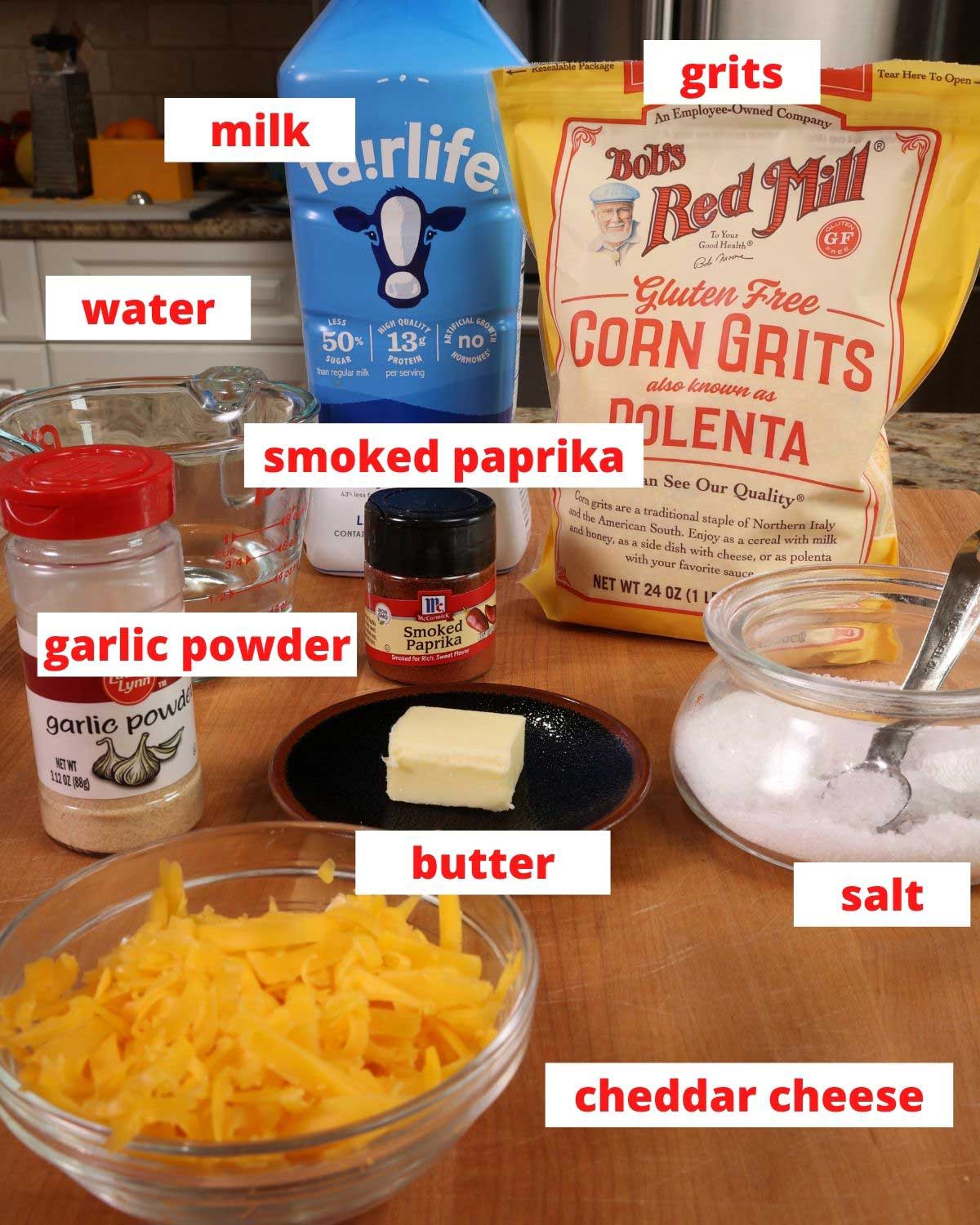 ingredients needed to make cheese grits on a brown table: cheese, grits, milk, spices,butter, and water.