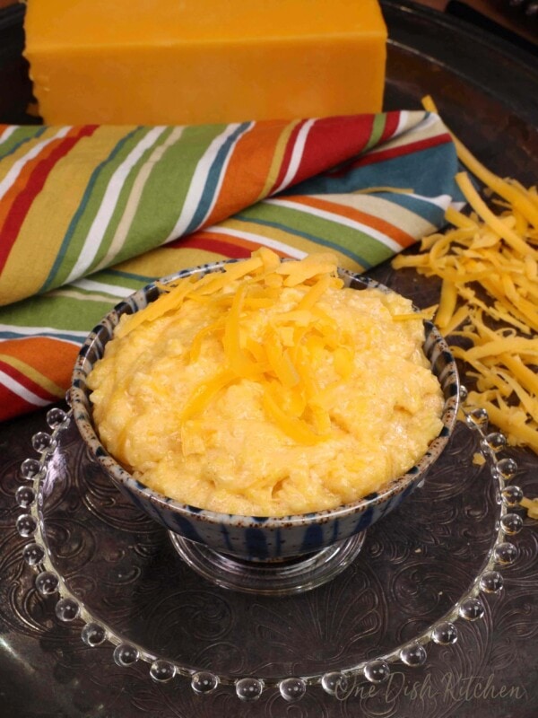 a small bowl of cheese grits next to shredded cheese and a large block of cheese in the background