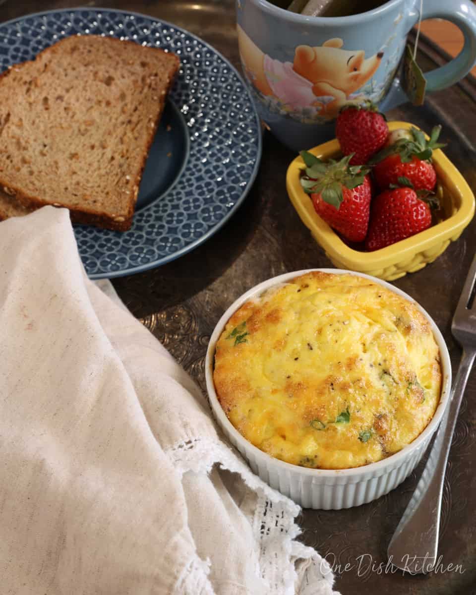 baked eggs with bacon on a tray next to toast and fruit.