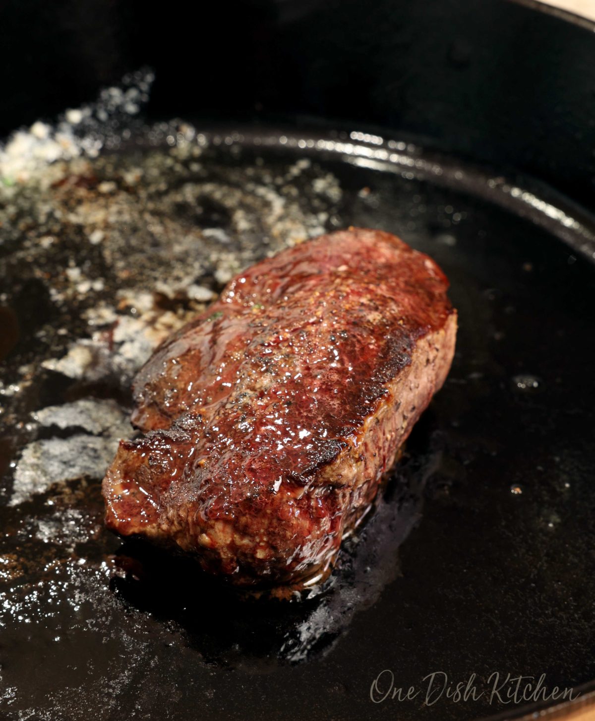 a filet mignon in a cast iron skillet with melted butter surrounding the steak.