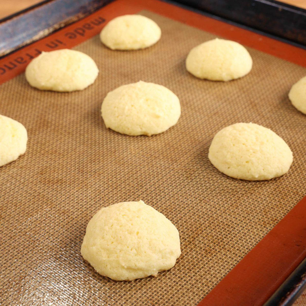 8 baked ricotta cookies on a silpat lined baking sheet.