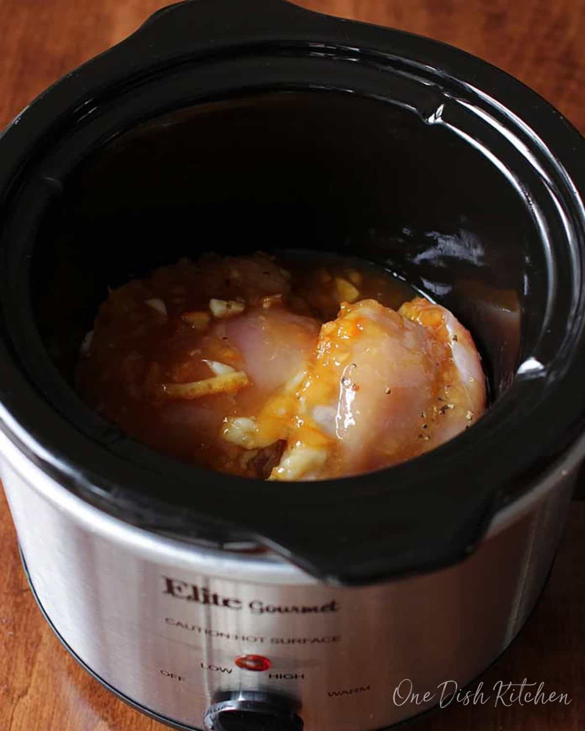 Raw chicken in an orange sauce in the base of a slow cooker.