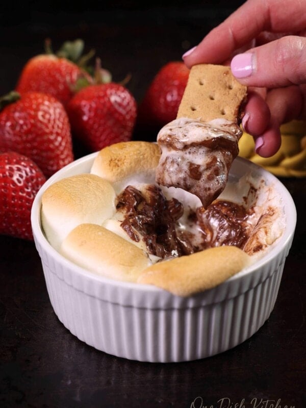 melted chocolate and toasted marshmallows in a small white ramekin with a graham cracker dipped into it.