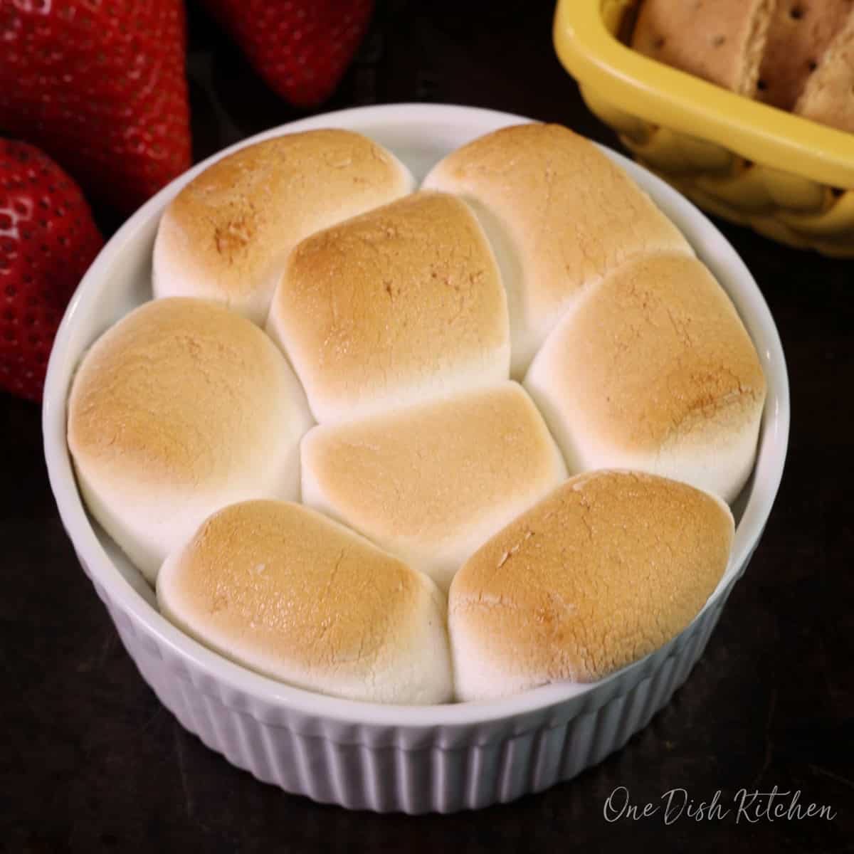 oven baked smores dip in a ramekin next to a bowl of graham crackers.