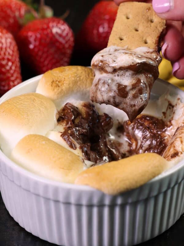 an oven baked smores dip in a ramekin with a graham cracker dipped into the melted chocolate.