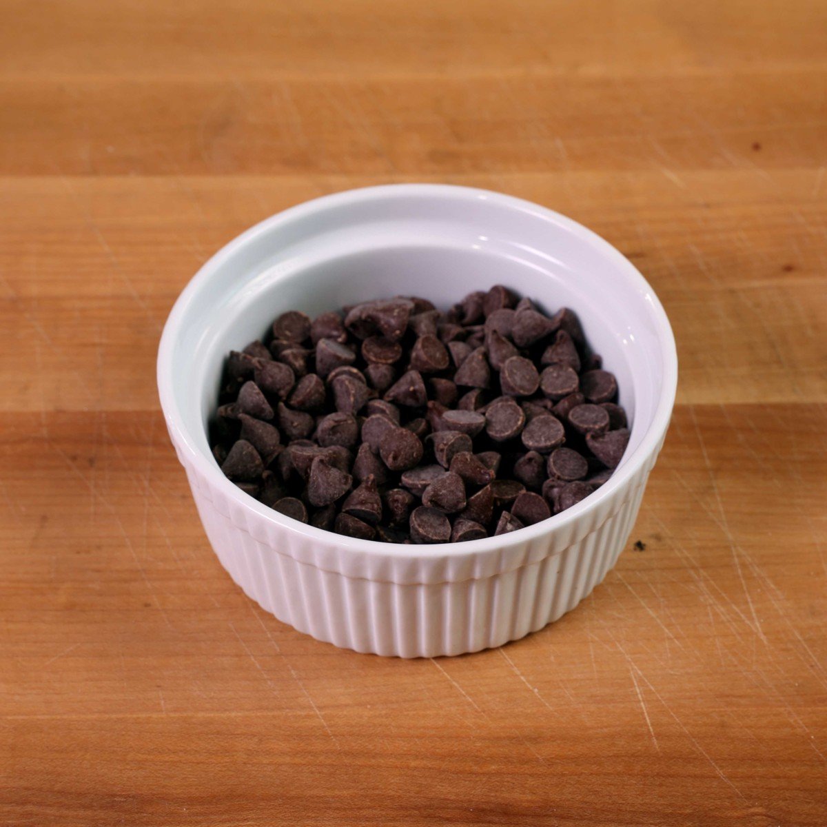 chocolate chips in a white ramekin on a brown table.