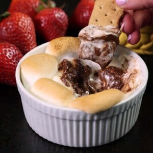 a mini s'mores dip on a black tray with a bowl of strawberries in the background