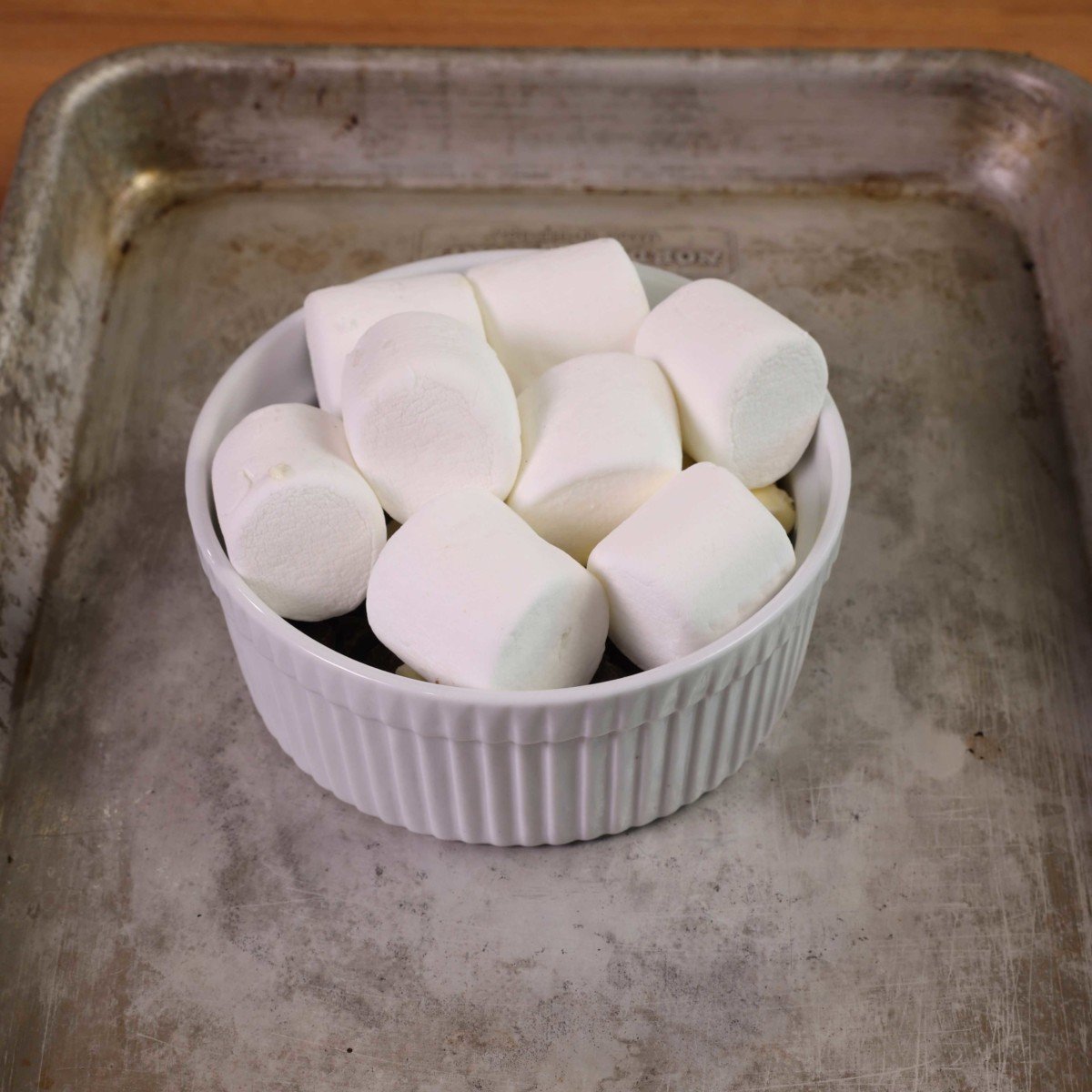 8 large marshmallows on top of chocolate chips in a white ramekin placed on top of a small baking sheet.
