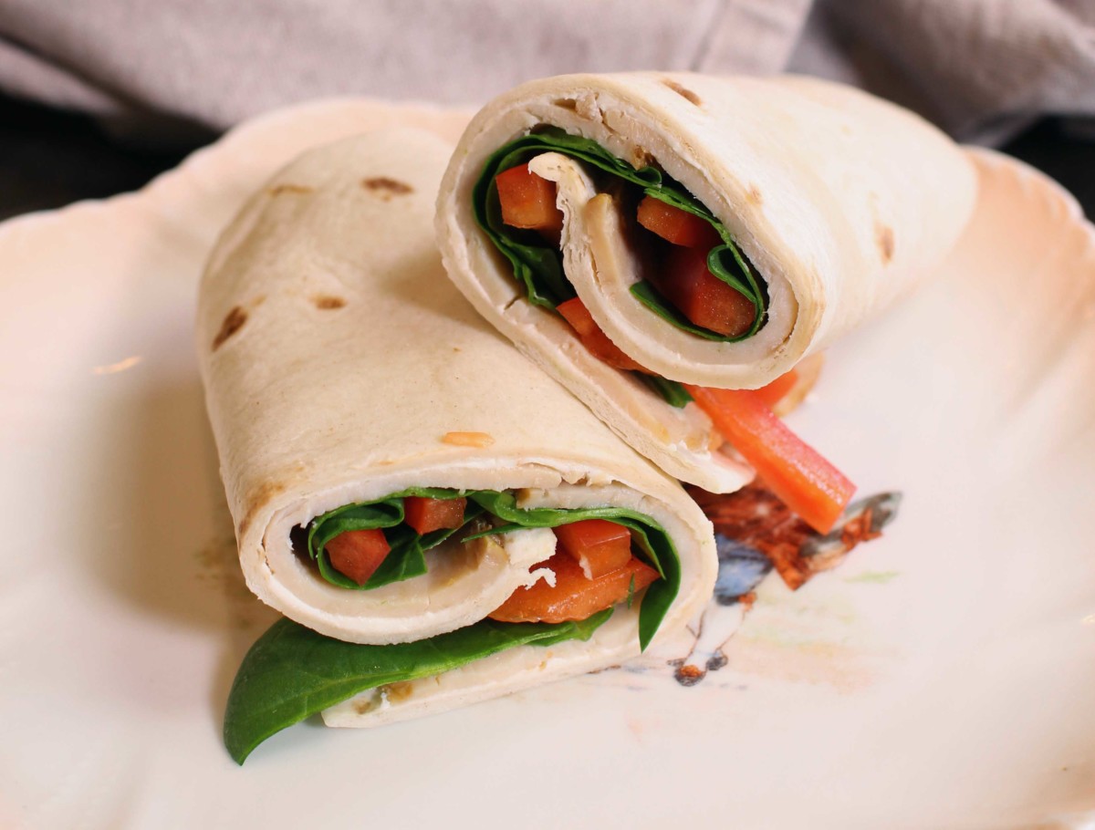 two pieces of a spinach and turkey wrap on a white plate.