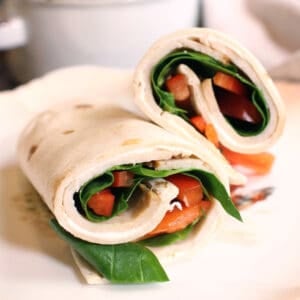 a turkey wrap with spinach and bell peppers on a white plate.