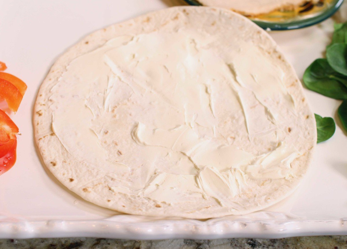 cream cheese spread over the top of a tortilla on a white plate.