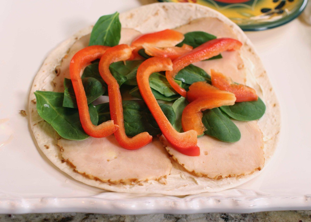 a flour tortilla topped with spinach and slices of red peppers.