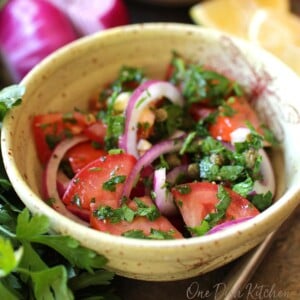 a mediterranean tomato salad in a yellow bowl next to red onions and lemons.