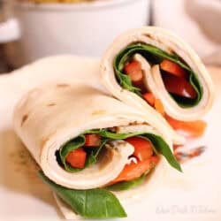 a turkey wrap filled with slices of deli turkey, spinach, and sliced red peppers.
