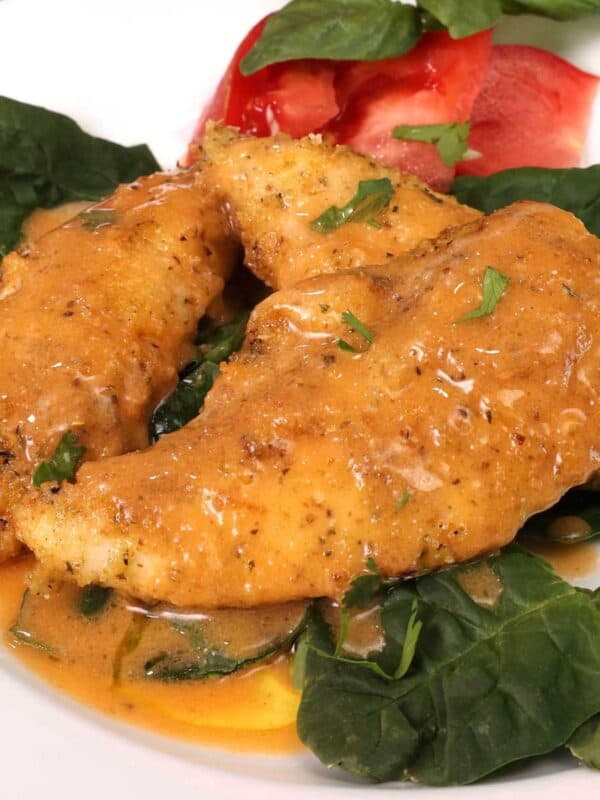breaded chicken tenderloins on a white plate topped with buffalo sauce.