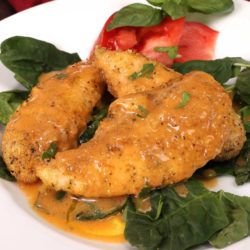 a white plate with three pieces of breaded chicken pieces on top of fresh spinach and buffalo sauce