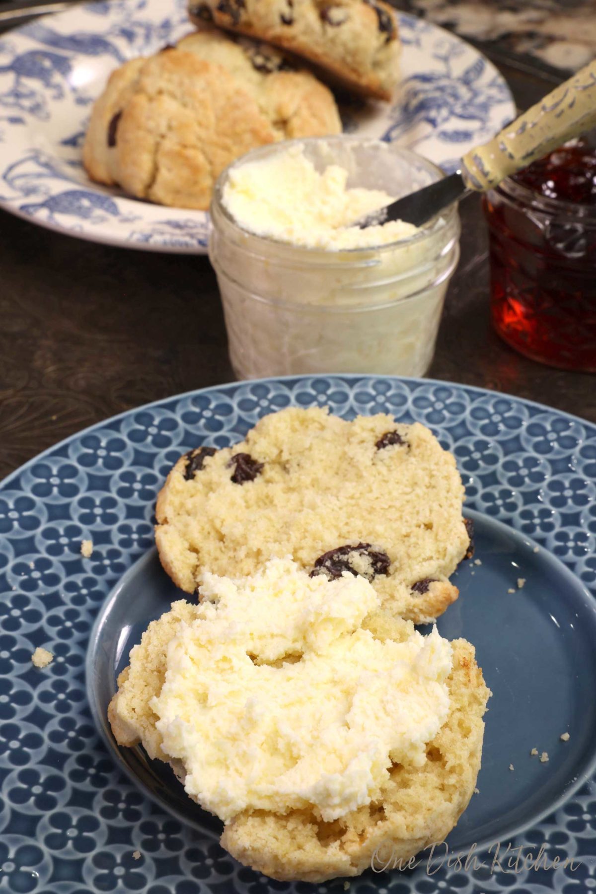 a scone sliced in half on a blue plate with clotted cream spread over one side of the scone