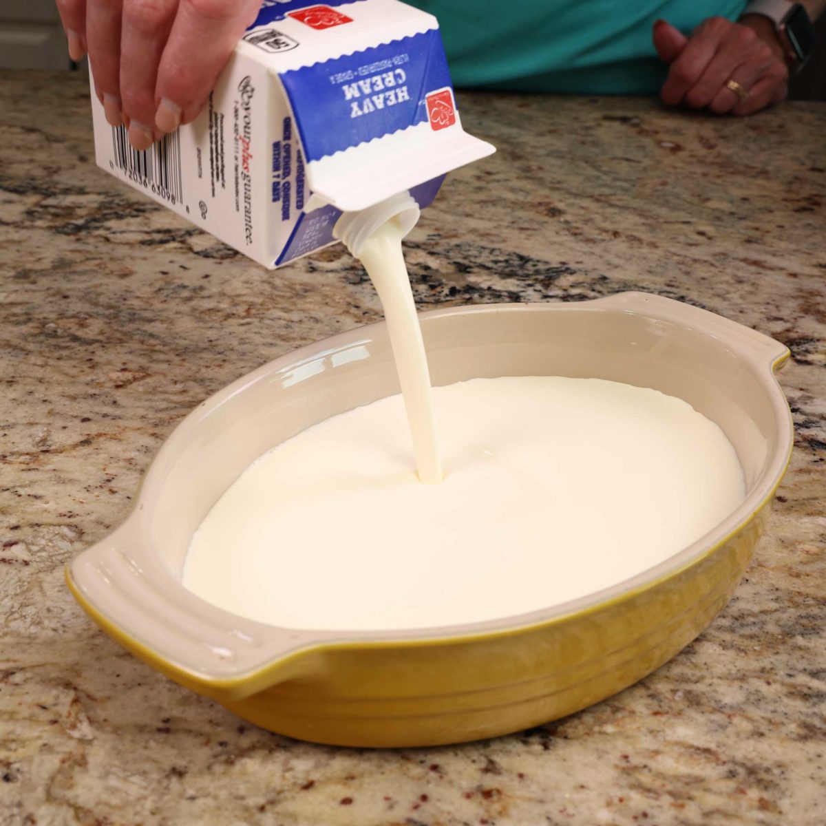 pouring heavy cream into an oval baking dish
