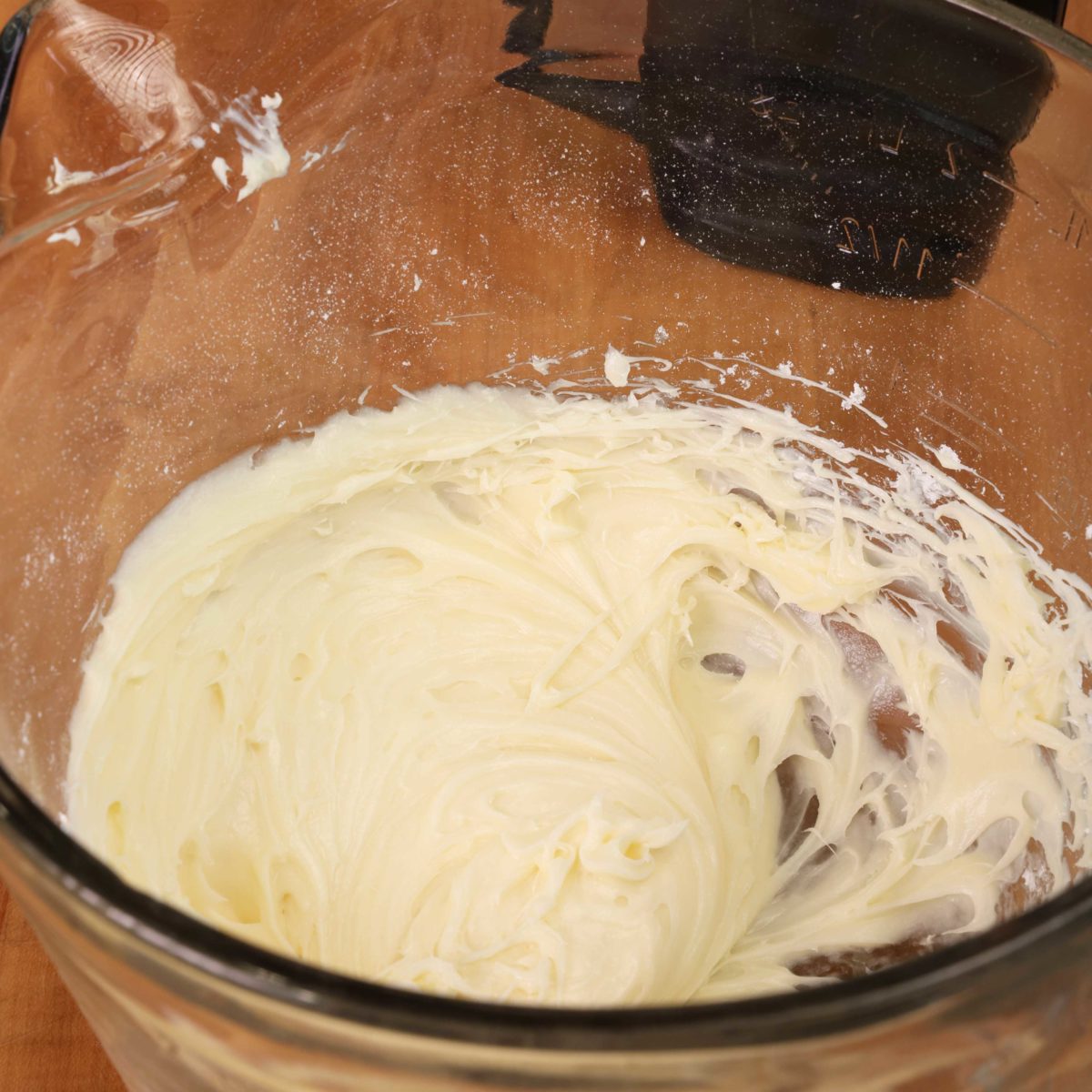 cream cheese frosting in a mixing bowl next to an electric mixer.