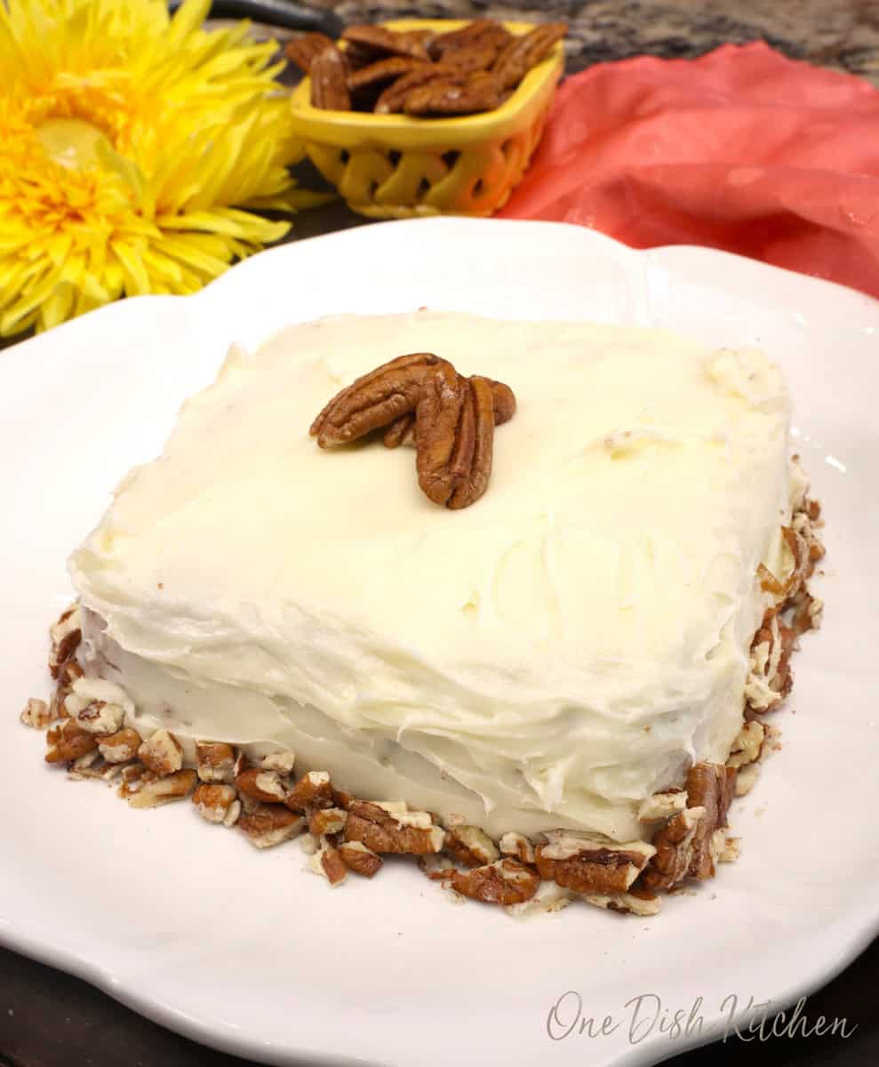 a small single layer hummingbird cake on a plate topped with pecans.