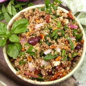 a small mediterranean quinoa salad in a yellow bowl with olives, feta and tomatoes.