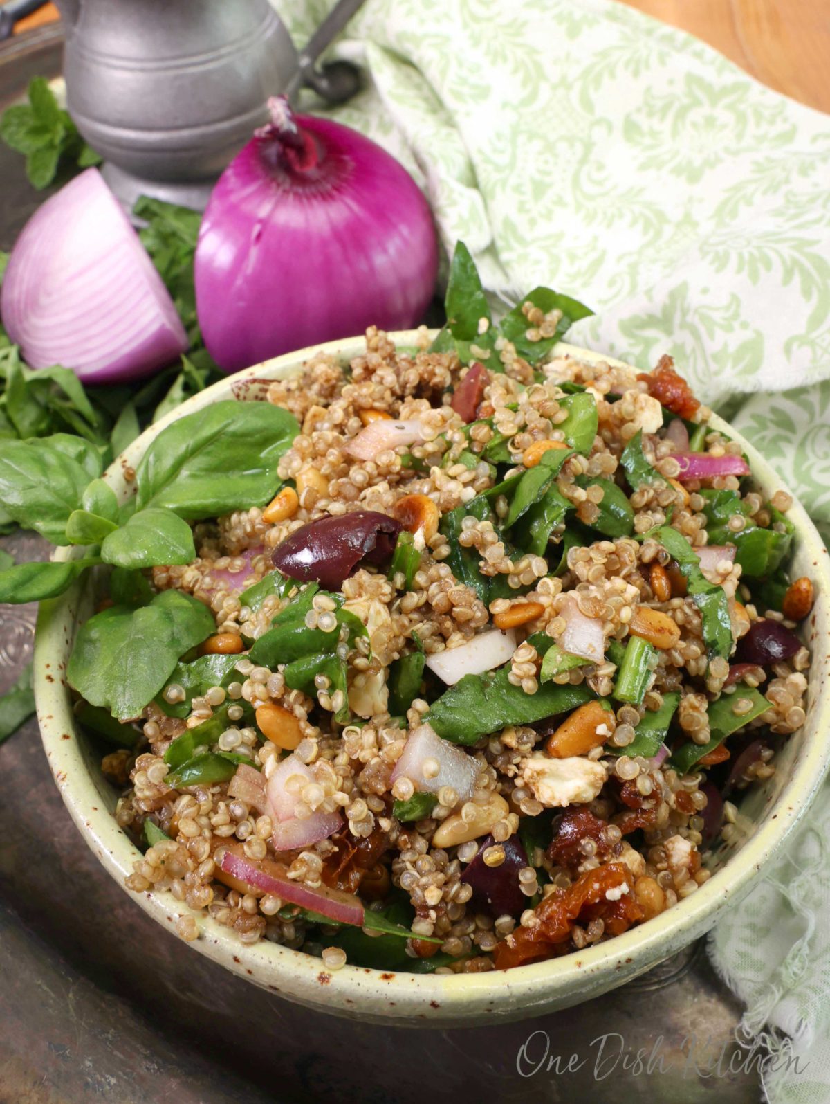 a yellow bowl filled with quinoa that is tossed with olives, feta, tomatoes, and onions on a silver tray.
