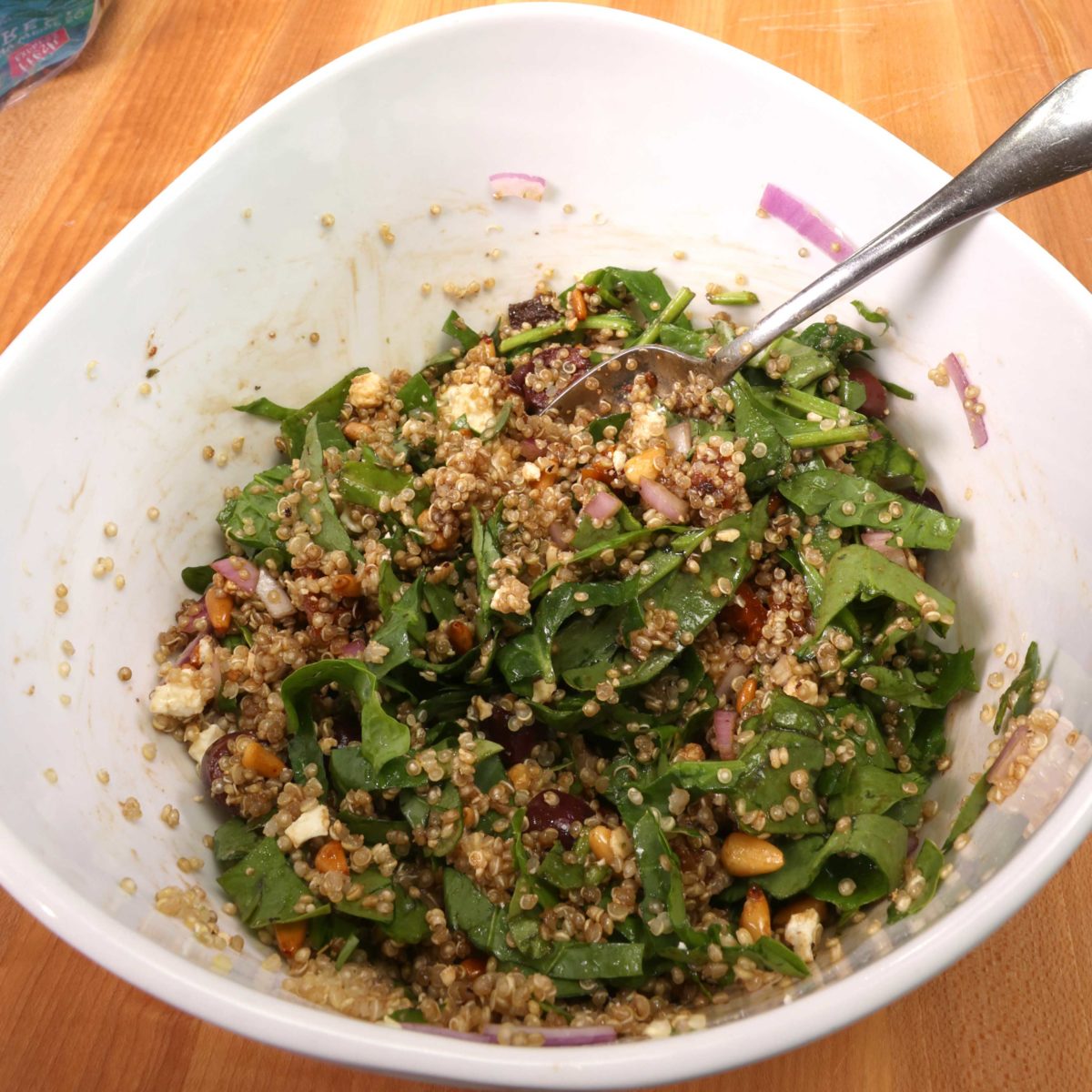 quinoa salad in a white bowl with spinach, pine nuts, and feta mixed in.