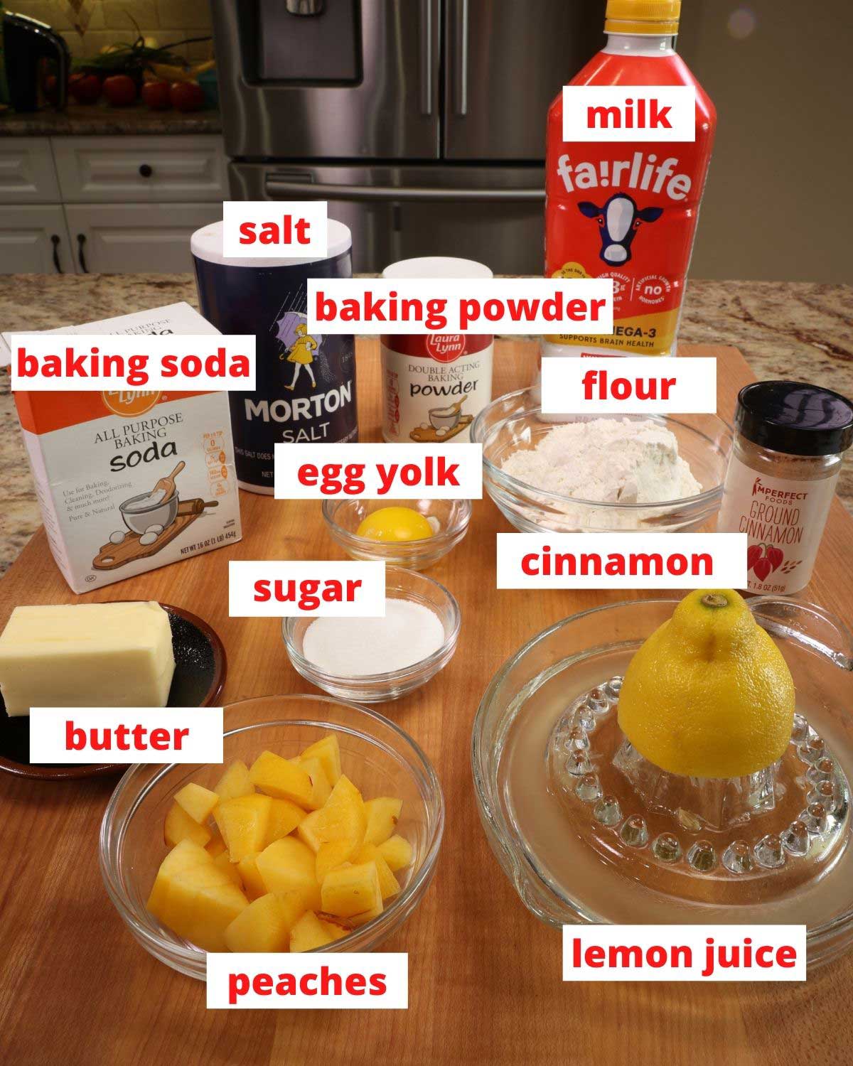 Ingredients for peach scones: diced peaches, butter, sugar, eggs, milk, flour and other pantry staples on a wooden cutting board.