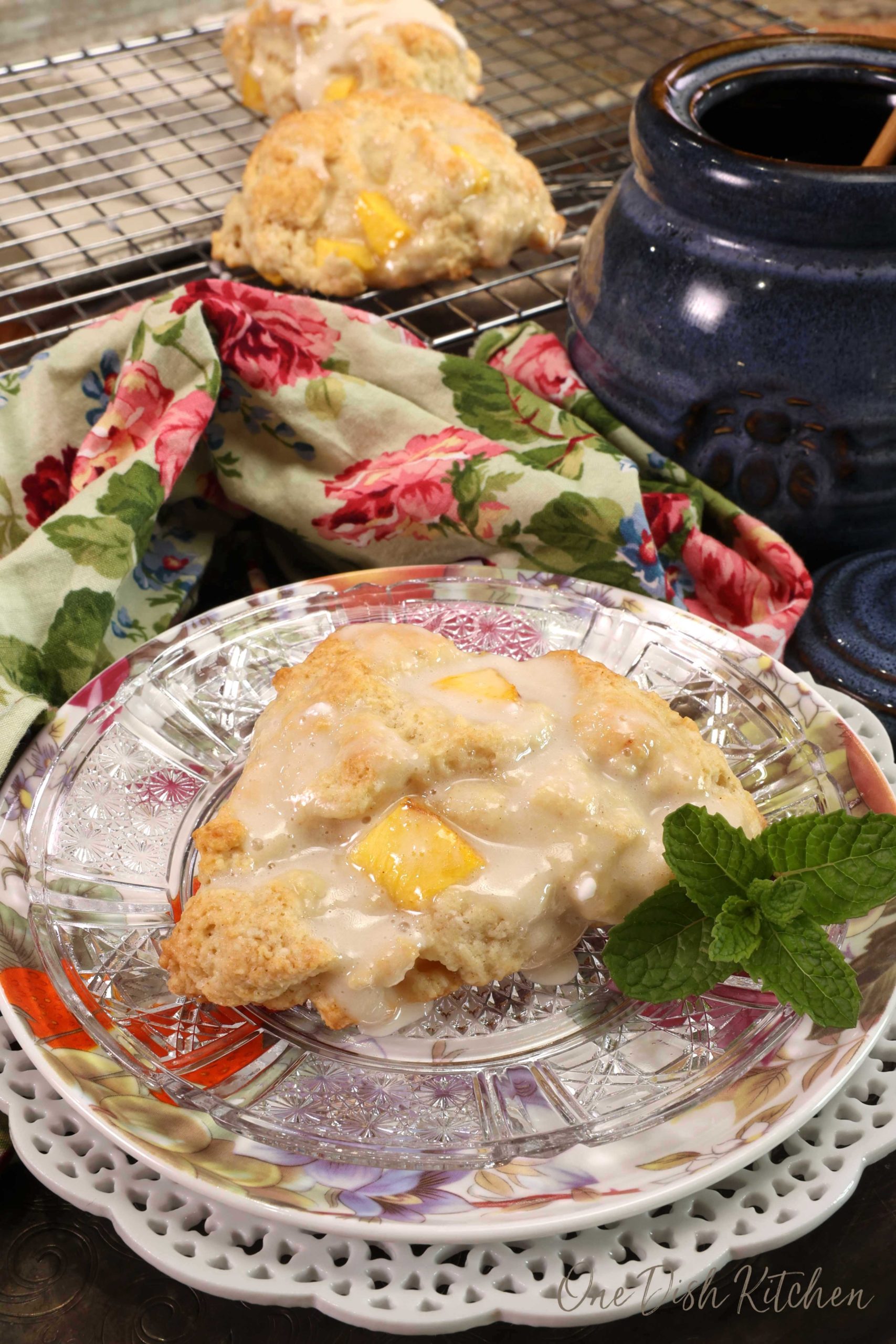 one peach scone on a floral plate next to a sprig of fresh mint and a flowered napkin in the background.