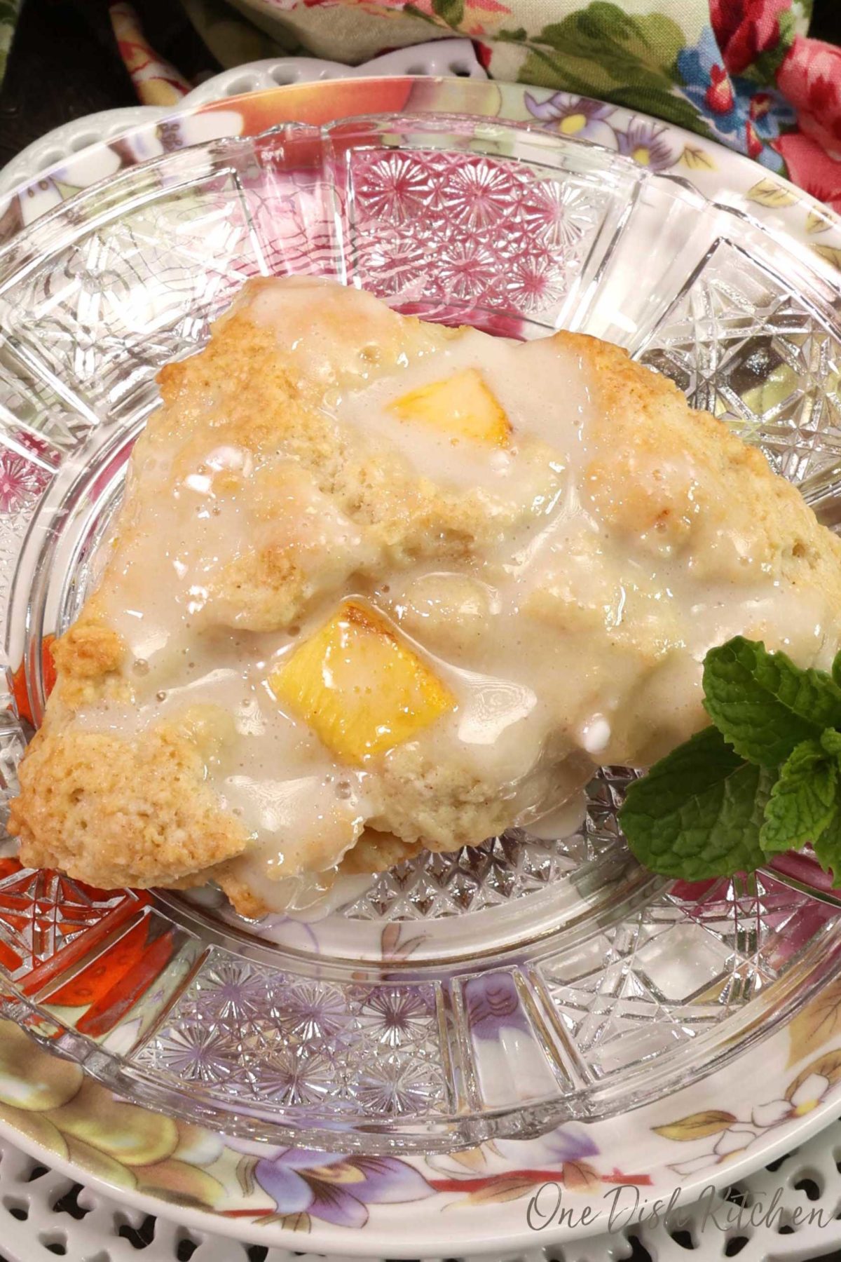 a peach scone topped with a honey glaze on a white plate next to a floral napkin.