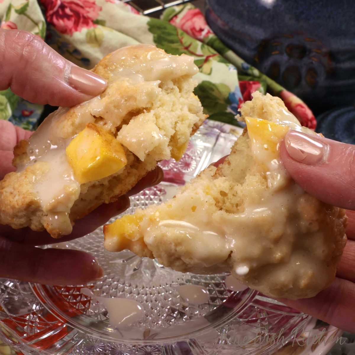 a hand holding a peach scone and breaking it in half over a plate.