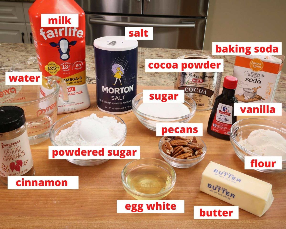 sugar, milk, cocoa, pecans, vanilla, egg whites, and other baking ingredients on a wooden cutting board.