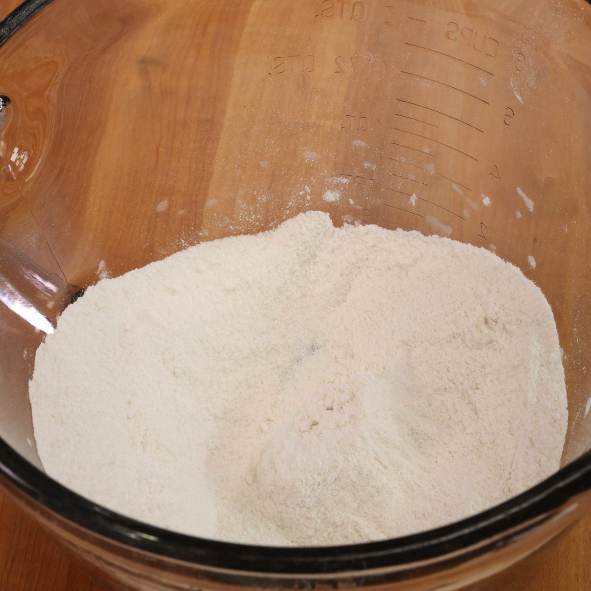 a mixing bowl filled with flour on a wooden cutting board.
