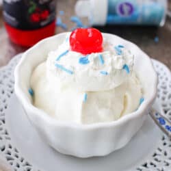 a white bowl filled with vanilla ice cream and topped with blue sprinkles and one maraschino cherry