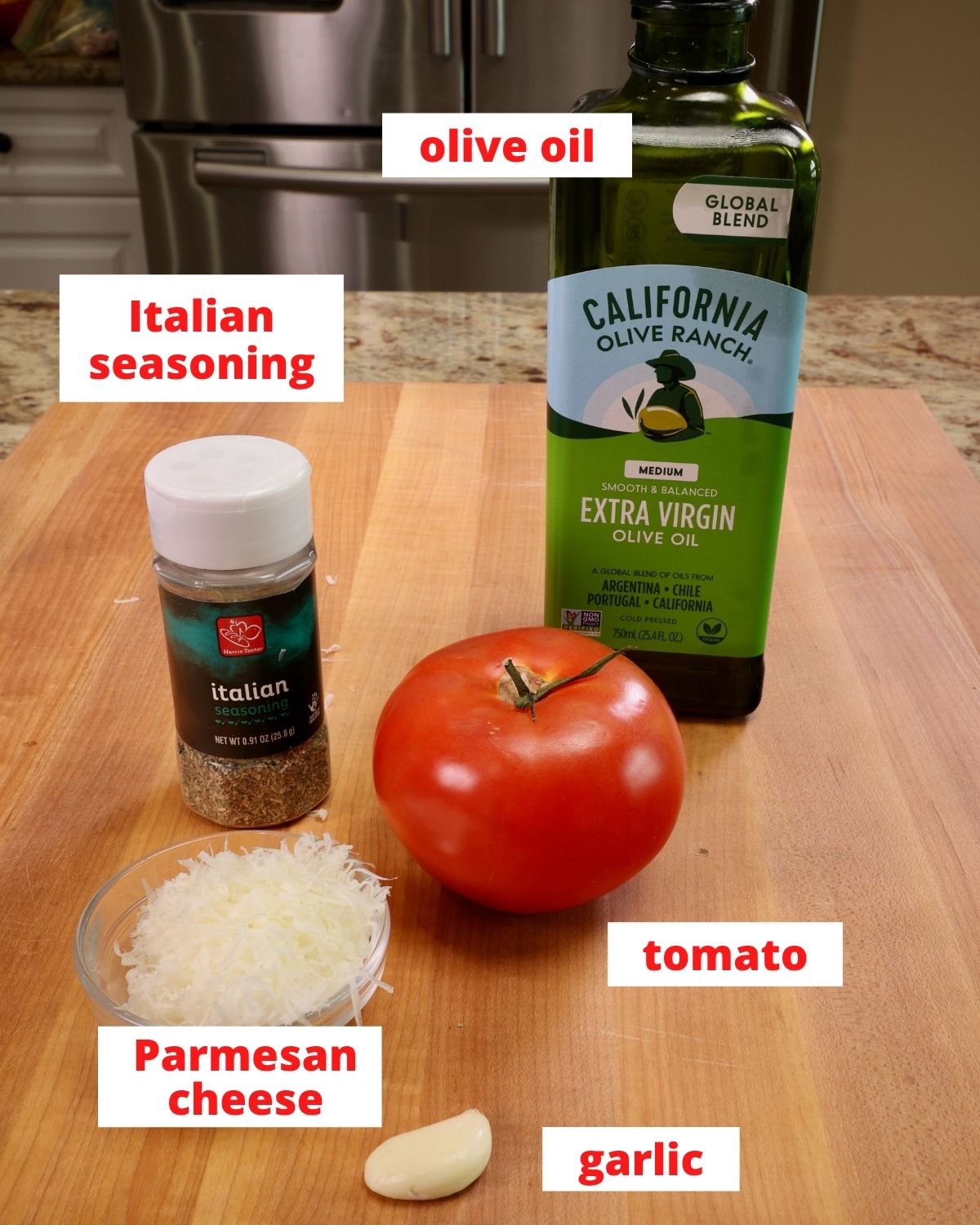 a tomato, olive oil, parmesan cheese, garlic, and italian seasoning on a wooden cutting board in a kitchen.