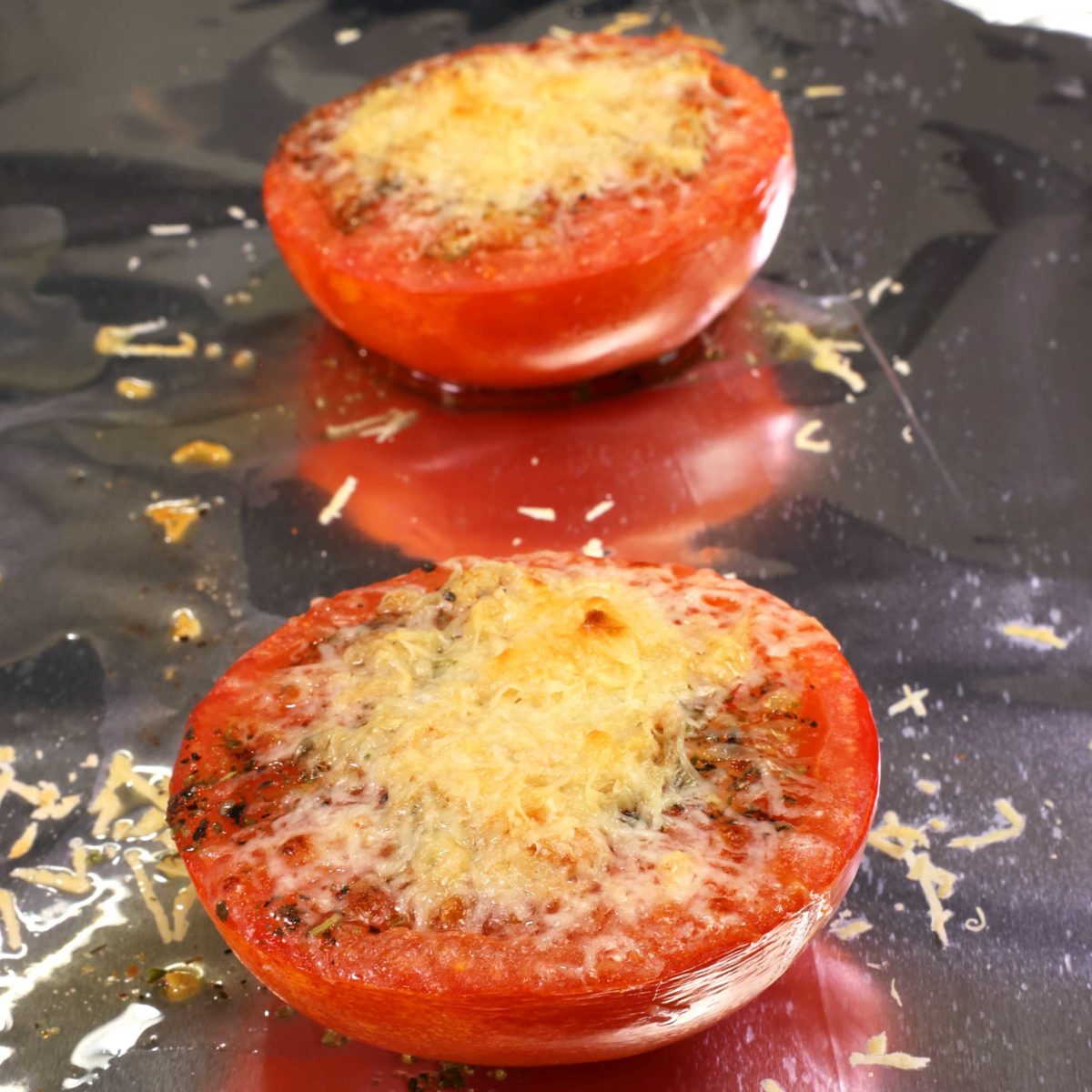two broiled tomatoes topped with melted cheese on a baking sheet.