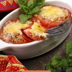 two broiled tomatoes in a white dish topped with melted cheese.
