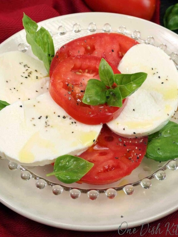 a small caprese salad topped with fresh basil on a white plate