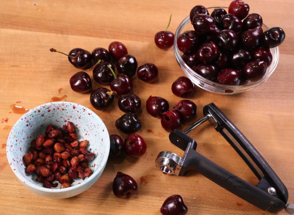a cherry pitter on a cutting board next to a pile of fresh cherries.